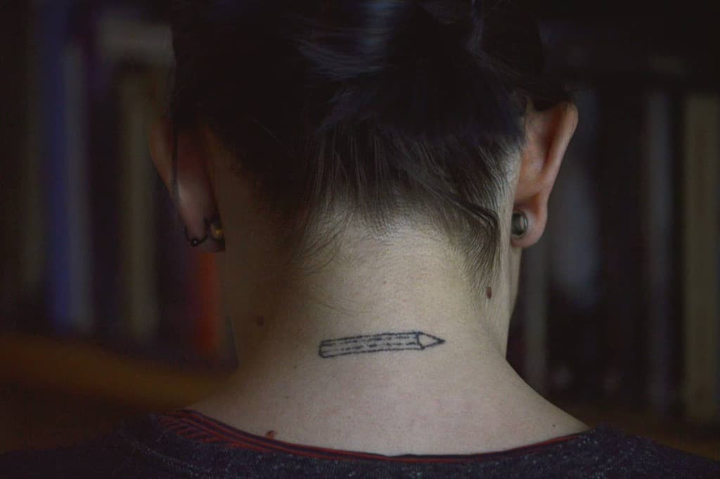 A tattoo of a pencil on the back of a neck