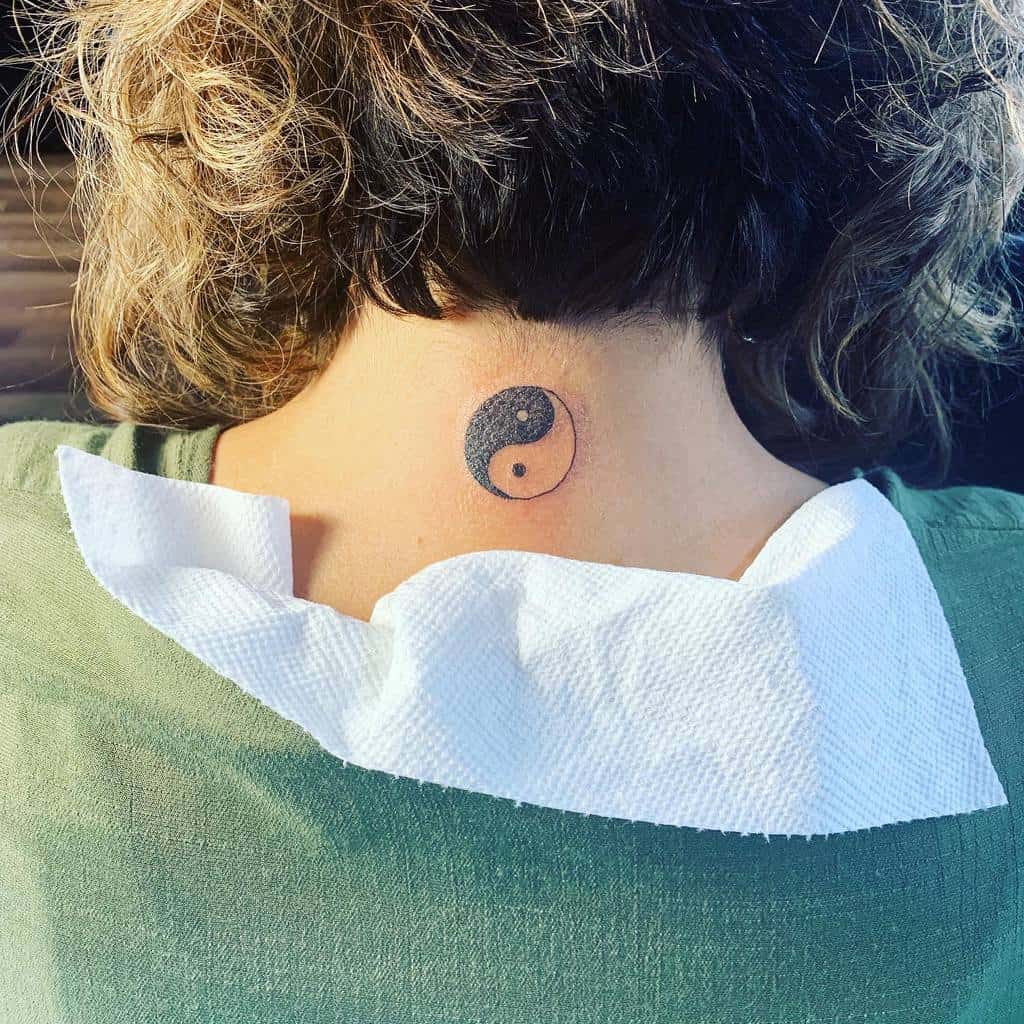 Yin-yang tattoo on the back of the neck of a person with short curly hair and a green top