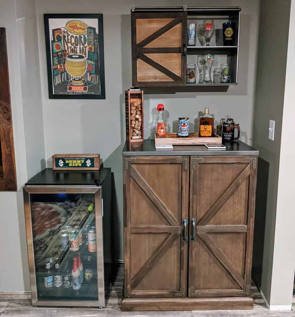 Small basement bar with rustic wood cabinetry, mini fridge, and sliding barn door shelving.