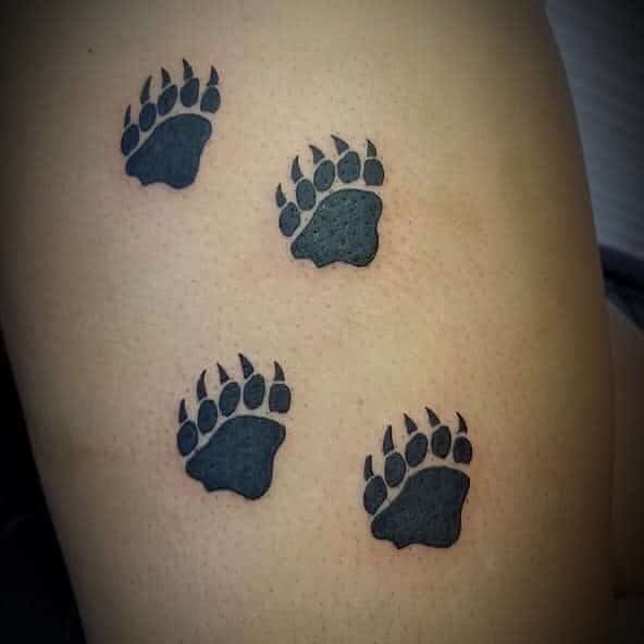 Four black bear paw prints tattooed on skin