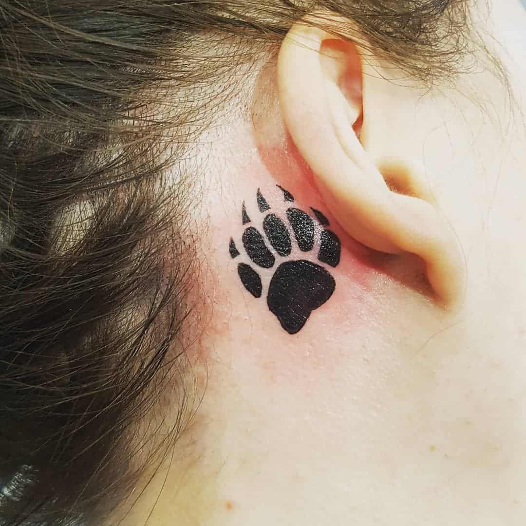 Tattoo of a black bear paw print behind someone's ear