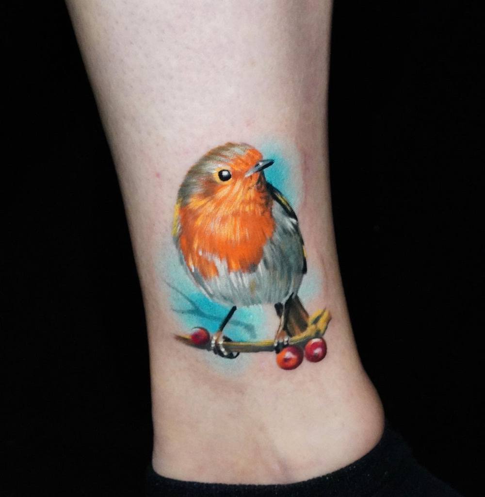 Colorful tattoo of a robin perched on a branch with berries, on an ankle