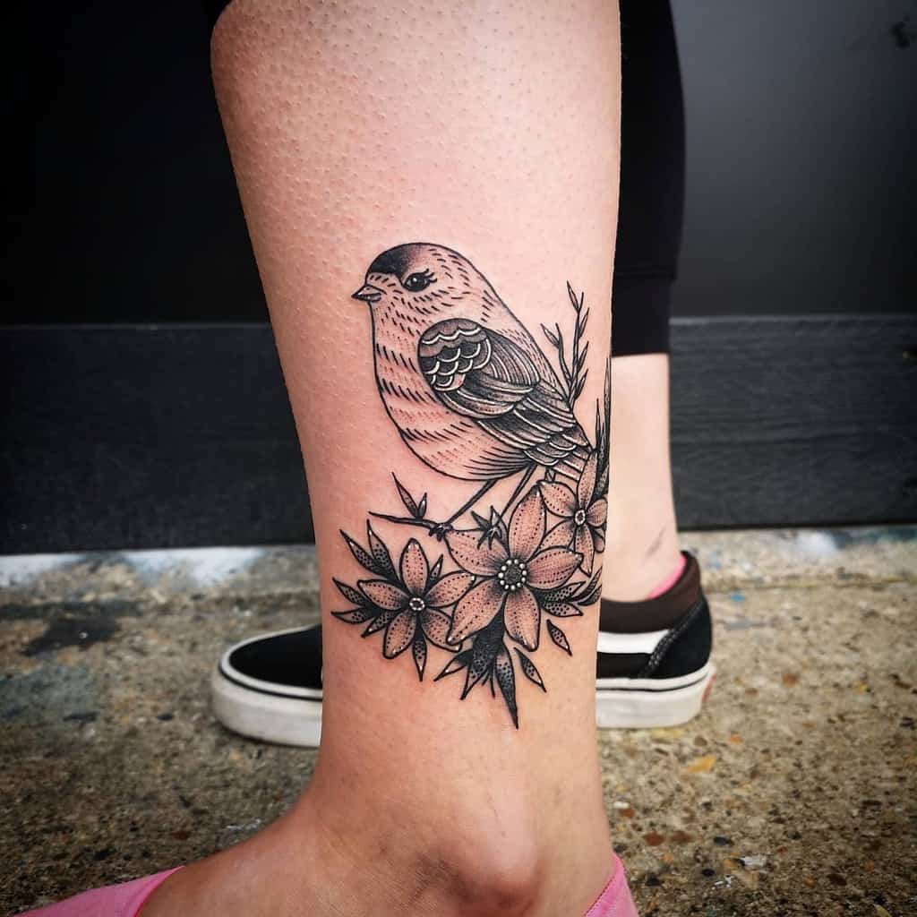 Black and grey bird tattoo perched on flowers on the back of a calf
