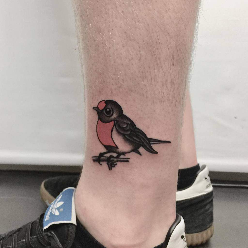 A tattoo of a bird with a red chest on an ankle