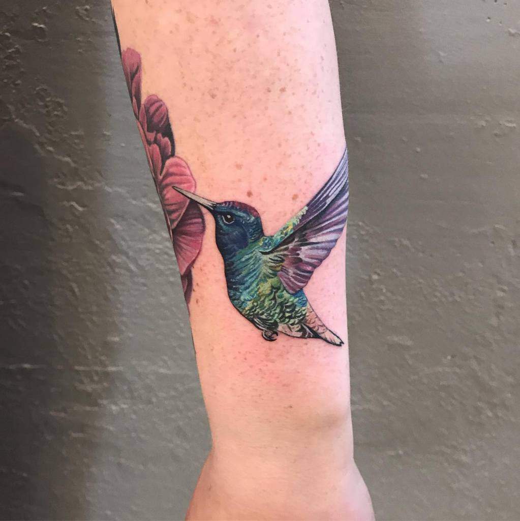 Colorful hummingbird tattoo on arm, sipping from a flower