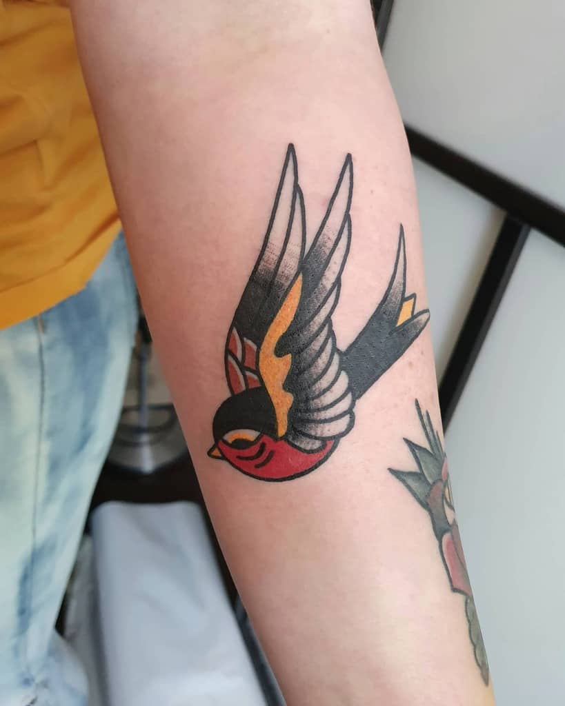 A colorful sparrow bird tattoo on an arm featuring bold lines and vibrant shades