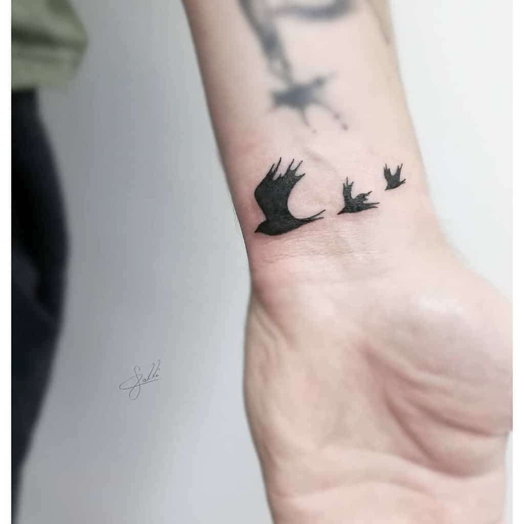 A wrist tattoo featuring three black ink flying birds