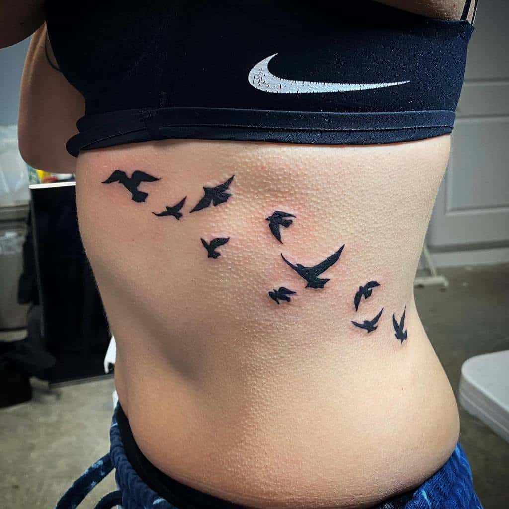 Rib tattoo featuring a flock of small black birds in flight, symbolizing freedom and movement