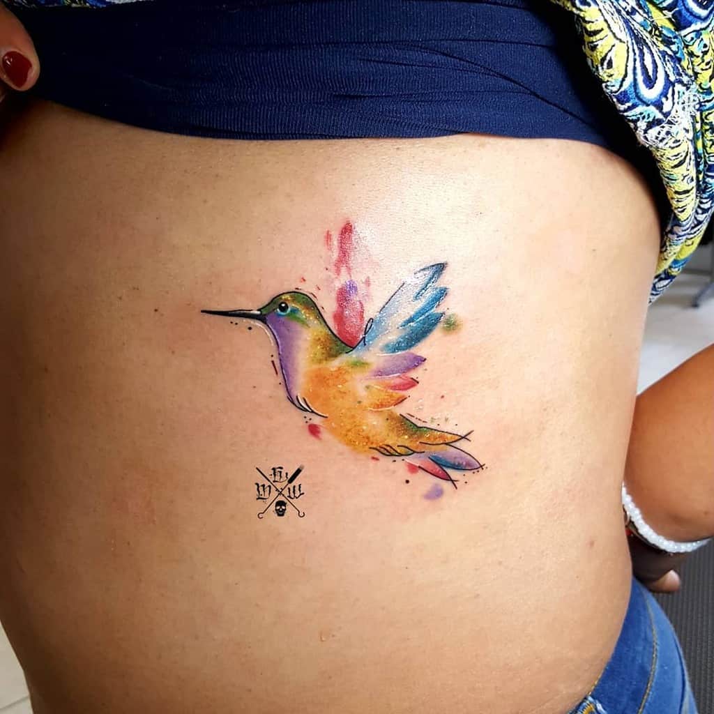 Small colorful watercolor hummingbird tattoo on a person's side torso