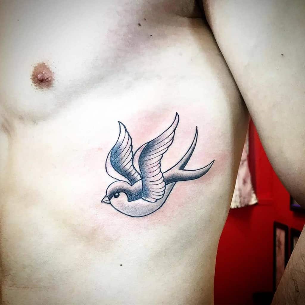 Tattoo of a flying swallow on a person's side torso