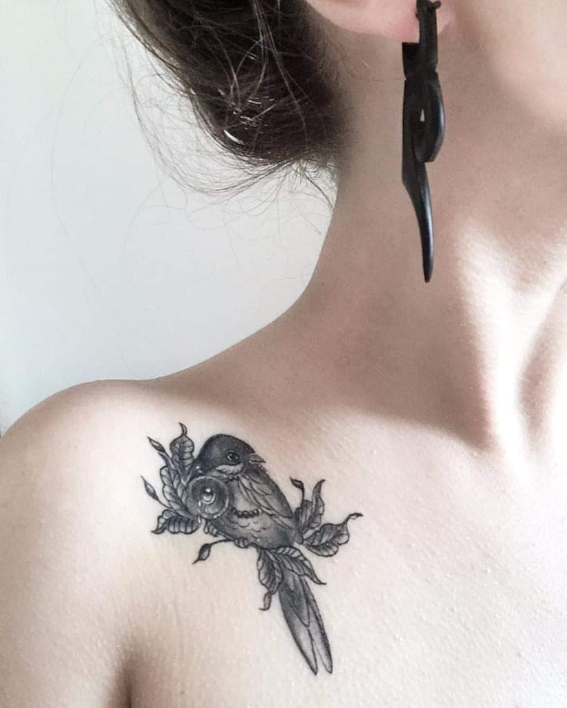 Shoulder tattoo of a delicate bird perched on a branch with detailed leaves, rendered in fine black ink