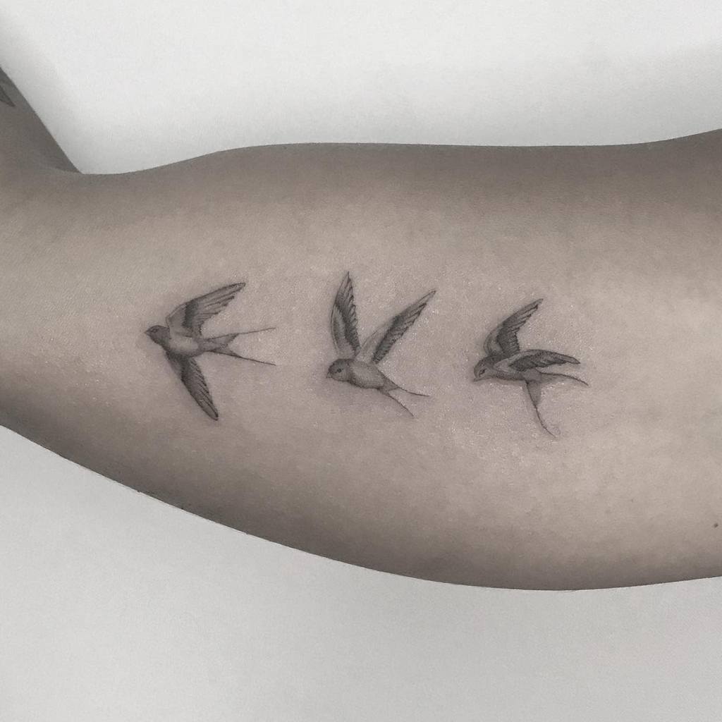 Forearm tattoo of three small swallows in flight against a light background