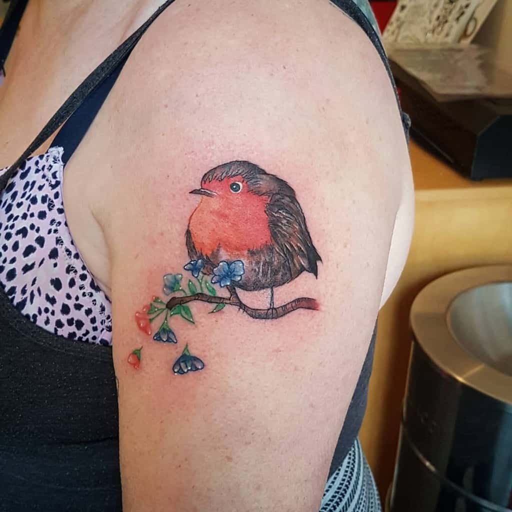 Tattoo of a robin with flowers on a woman's upper arm