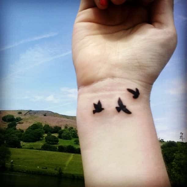 Wrist with small three black bird tattoos 