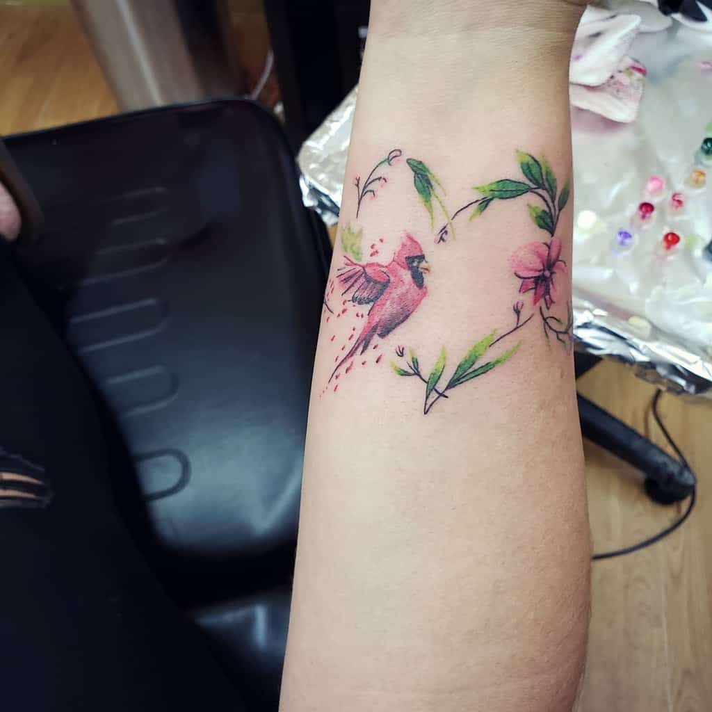 Wrist tattoo of a pink bird and flowers forming a heart shape