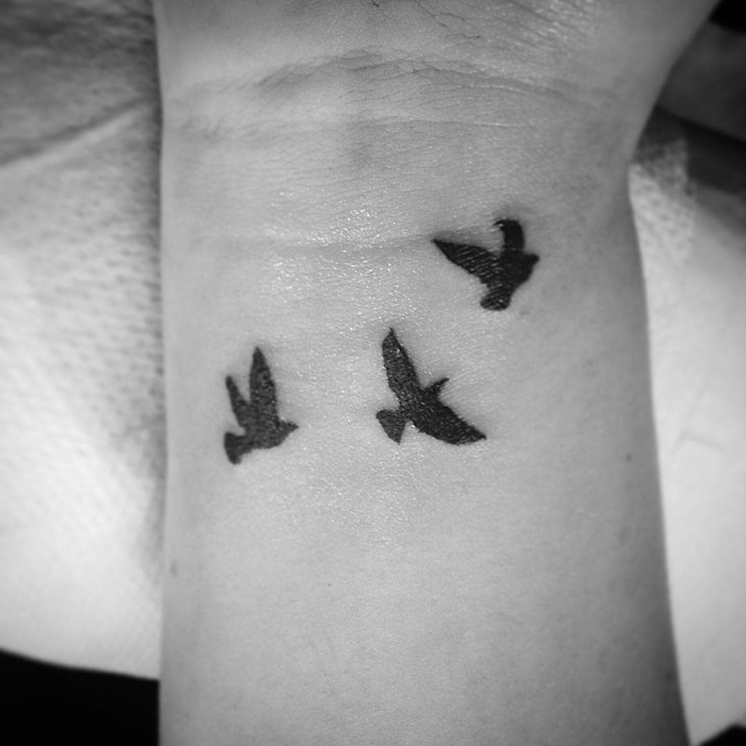 Black and white tattoo of three flying birds on a wrist