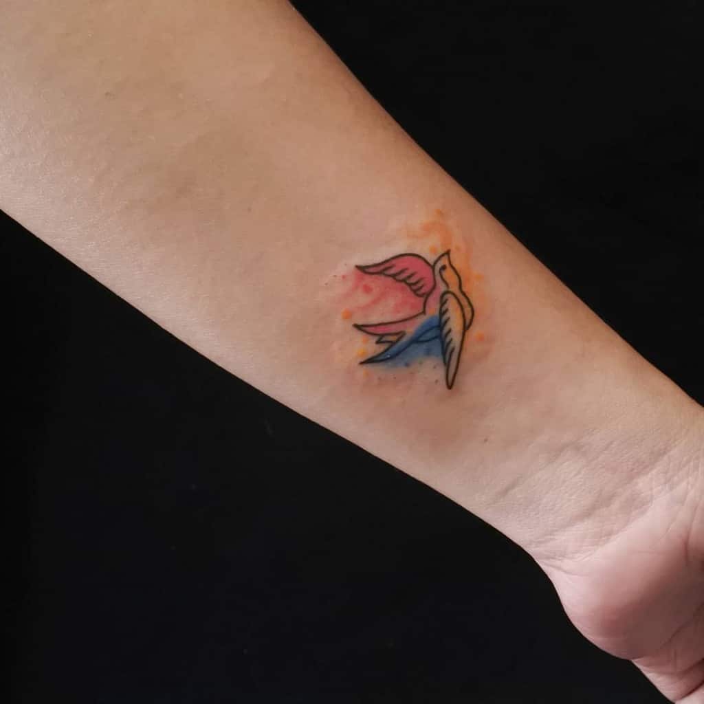 Colorful wrist tattoo of a bird in flight with vibrant pink, blue, and orange watercolor accents