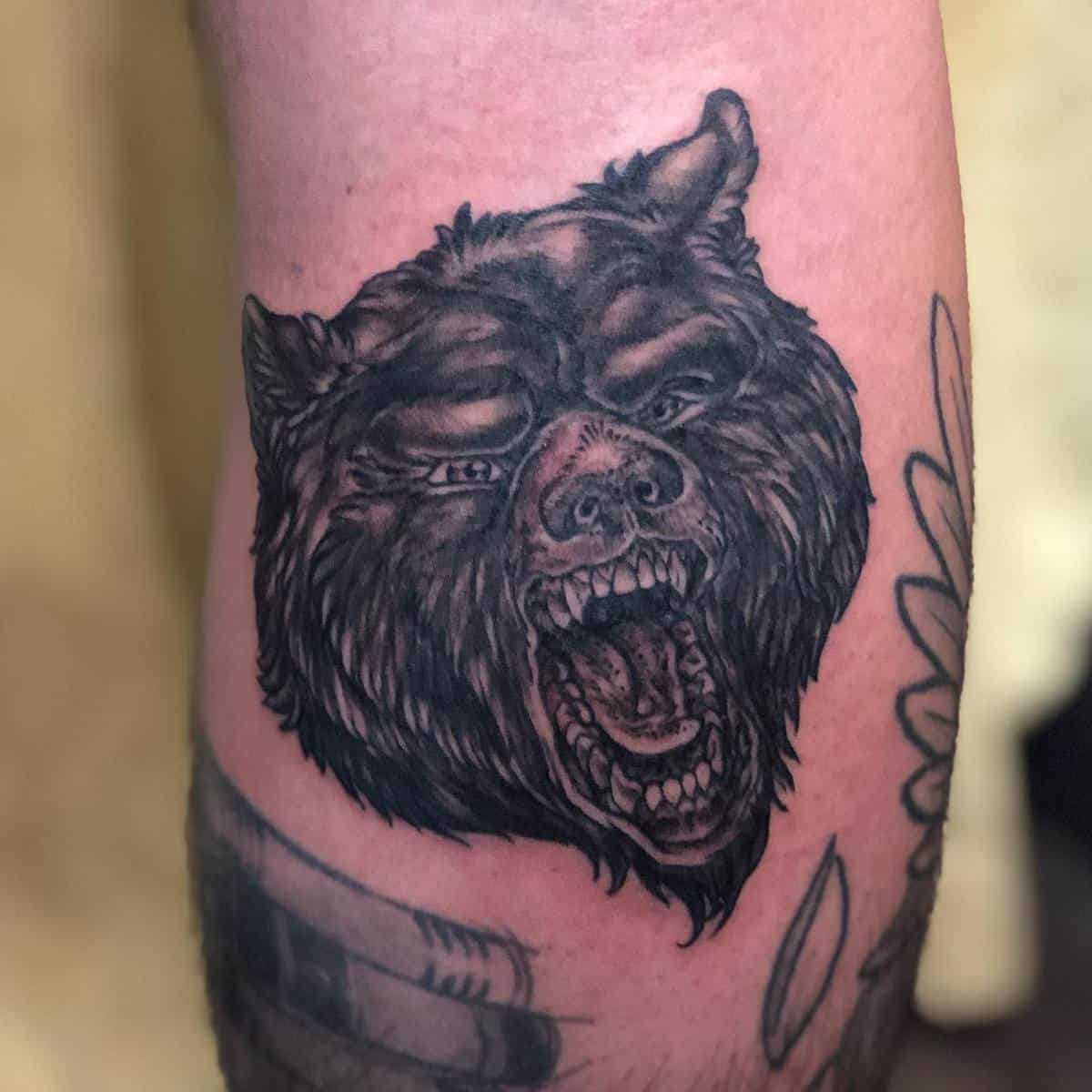 Tattoo of a fierce bear head roaring on a person's arm