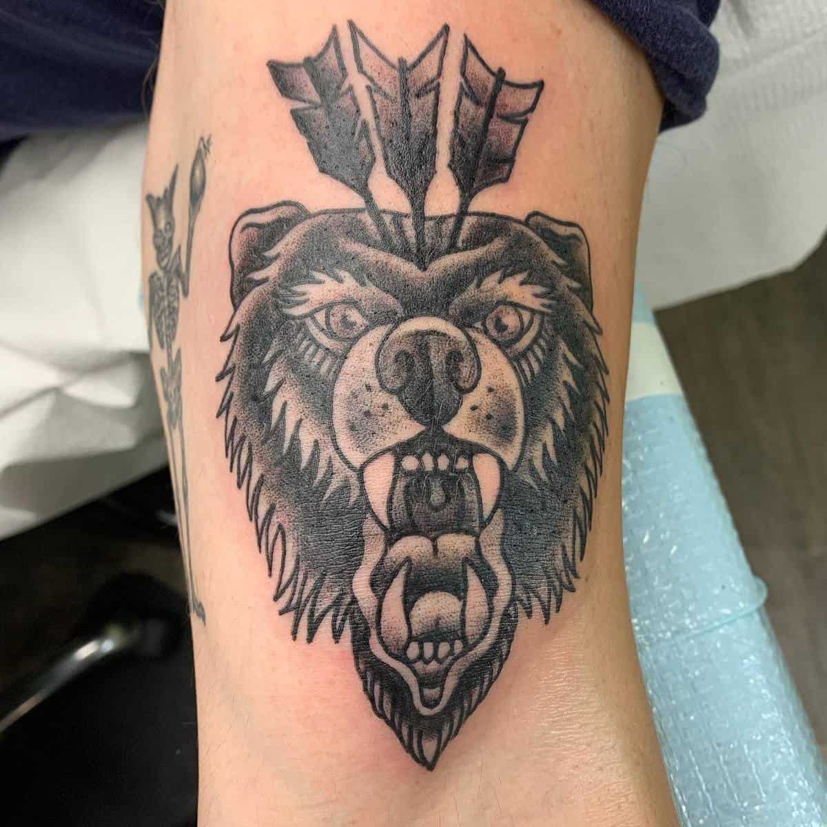 Tattoo of an enraged bear's head with arrows piercing through it on a person's arm