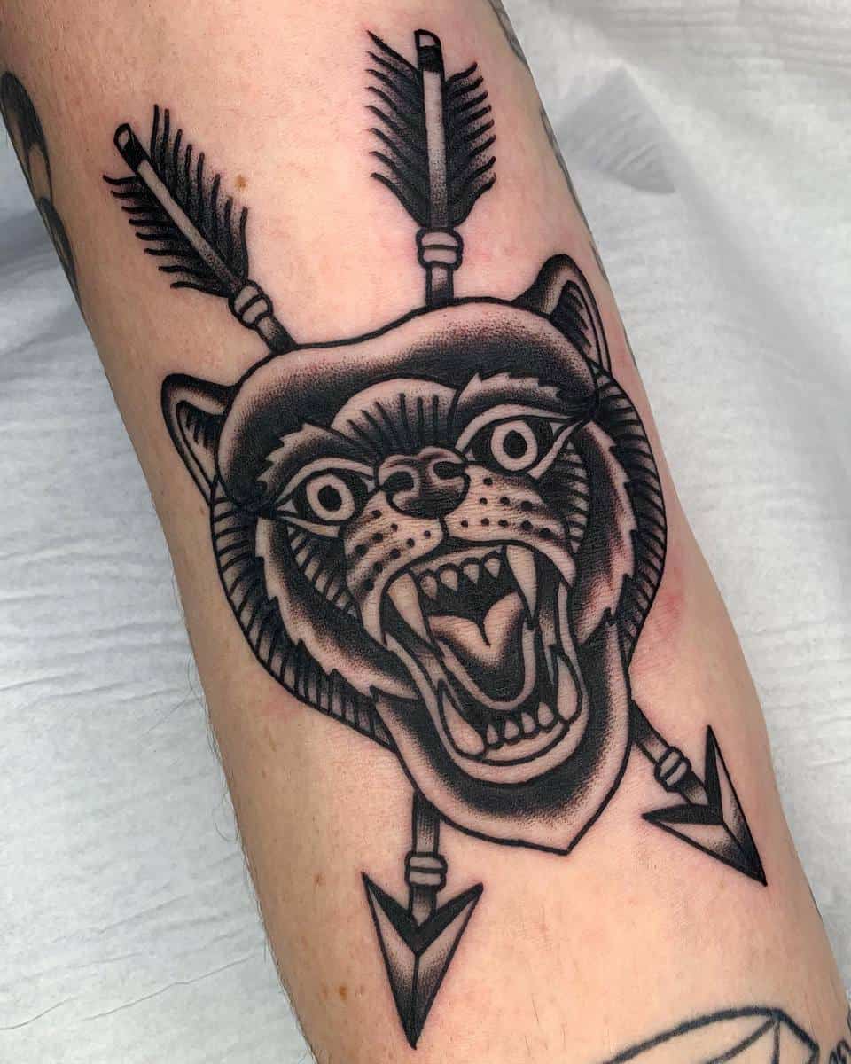 Tattoo of a roaring bear's head with arrows piercing through its ears