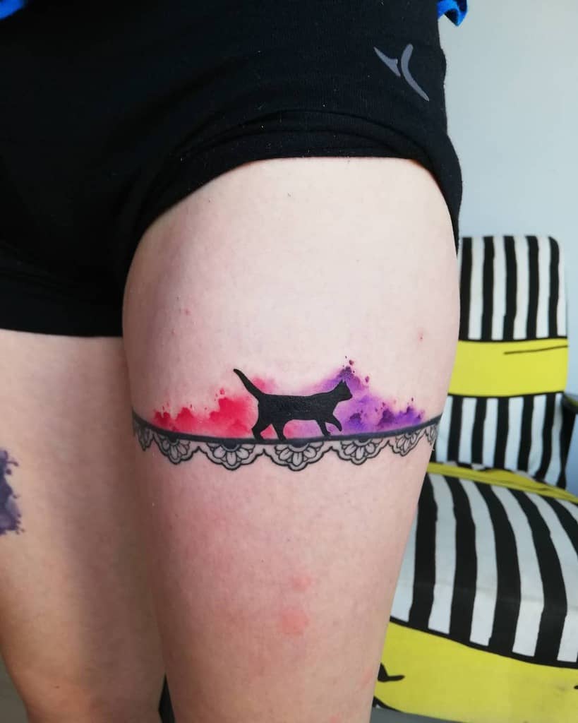Tattoo of a cat silhouette walking with a vibrant, colorful background on a person's thigh