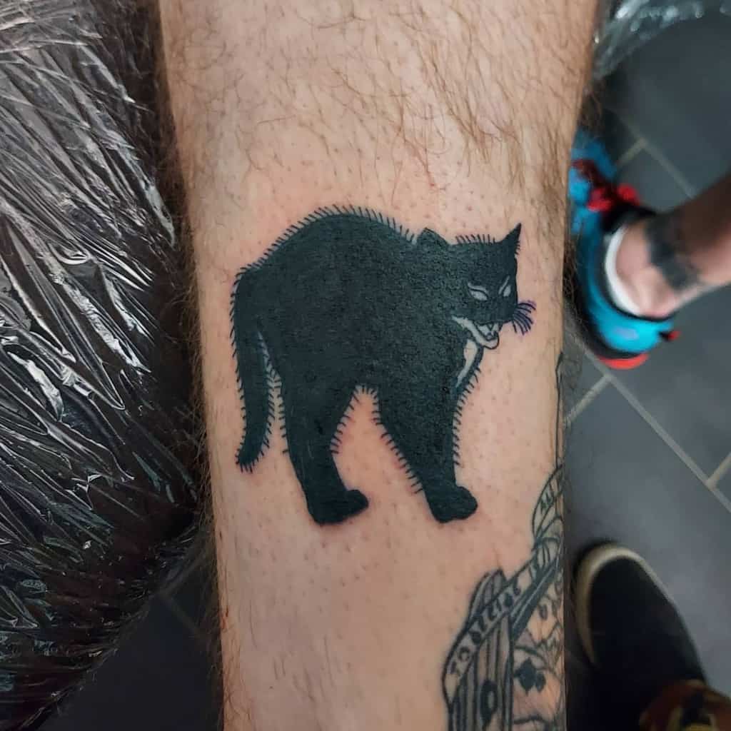 Black cat tattoo on a person's leg, featuring a menacingly arched and hissing feline