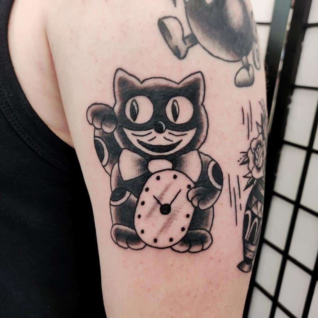 Tattoo of a vintage-style cat clock with big eyes and a bowtie on an upper arm