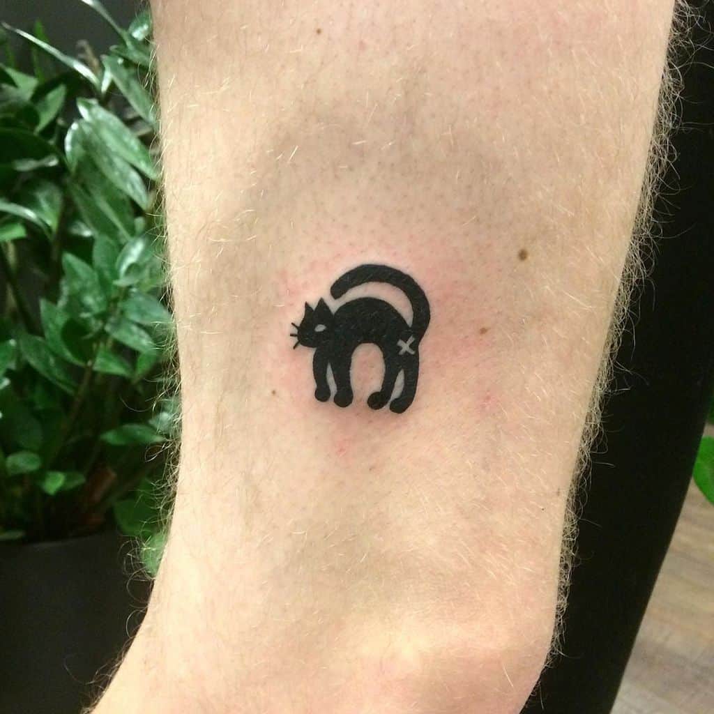 Simple black silhouette tattoo of a cat with an arched back, featuring a minimalistic and bold design