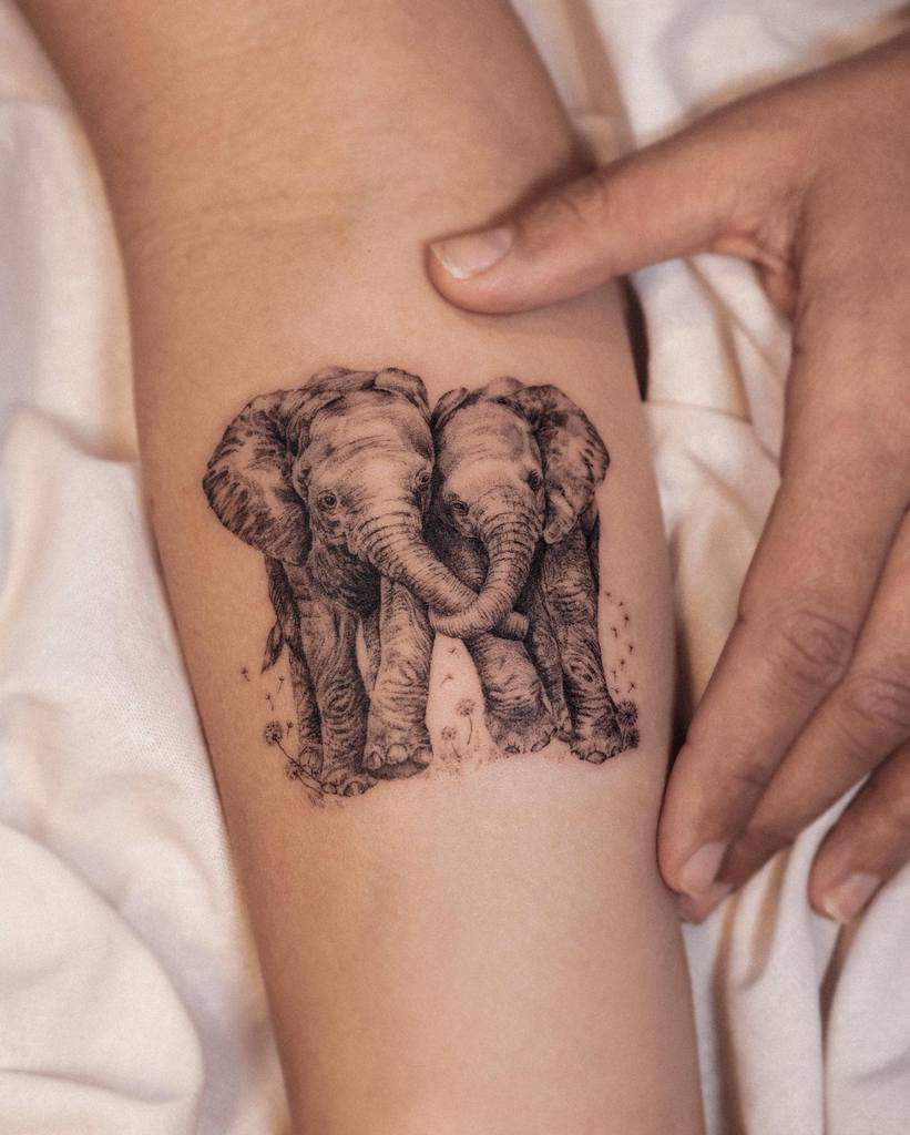 Close-up of a tattoo of two elephants on an arm, with a hand gently touching the inked design