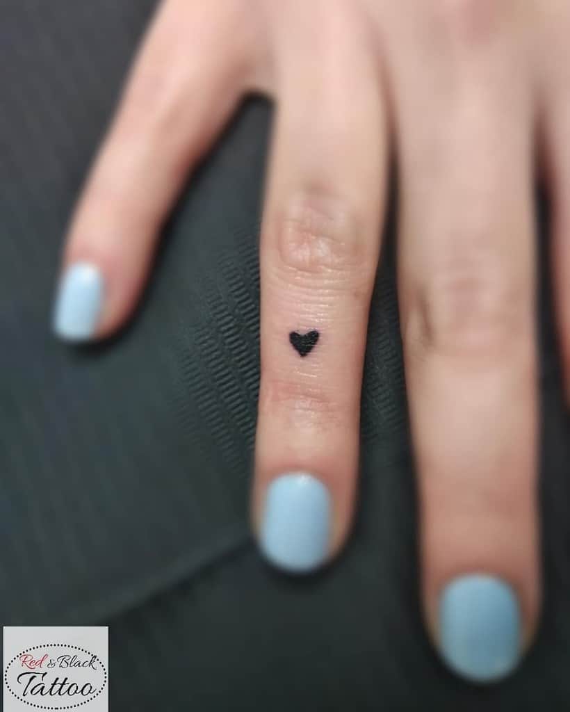 Close-up of a small black heart tattoo located on the side of a finger, creating a subtle yet stylish look