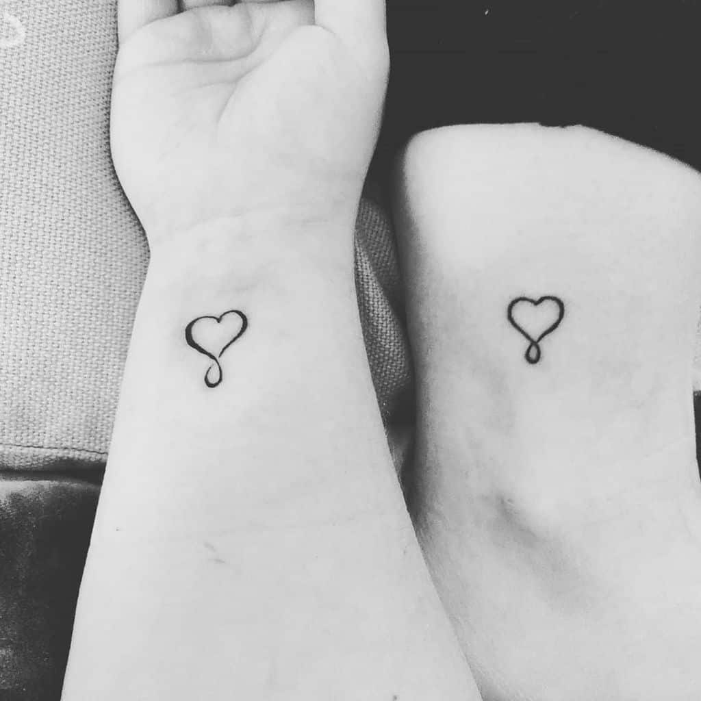 Two wrists side by side, each with a small heart tattoo connected to an elegant swirl, symbolizing unity and affection in a minimalist design
