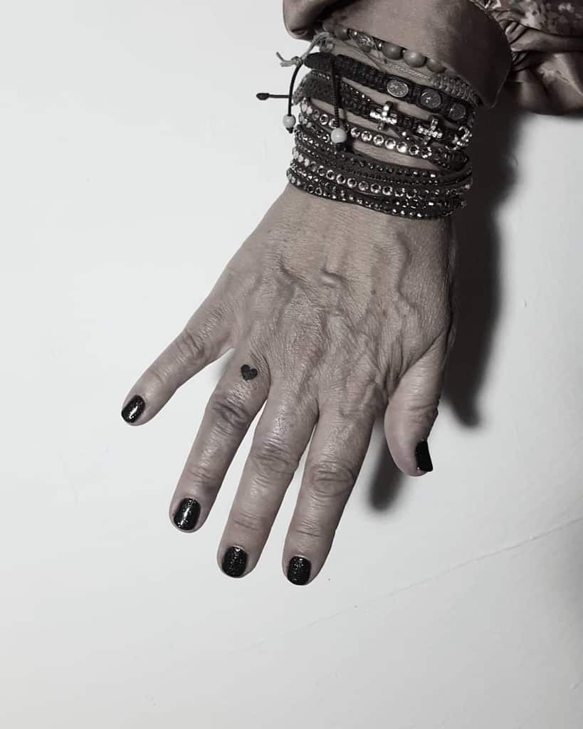 Small black heart tattoo on the side of a finger