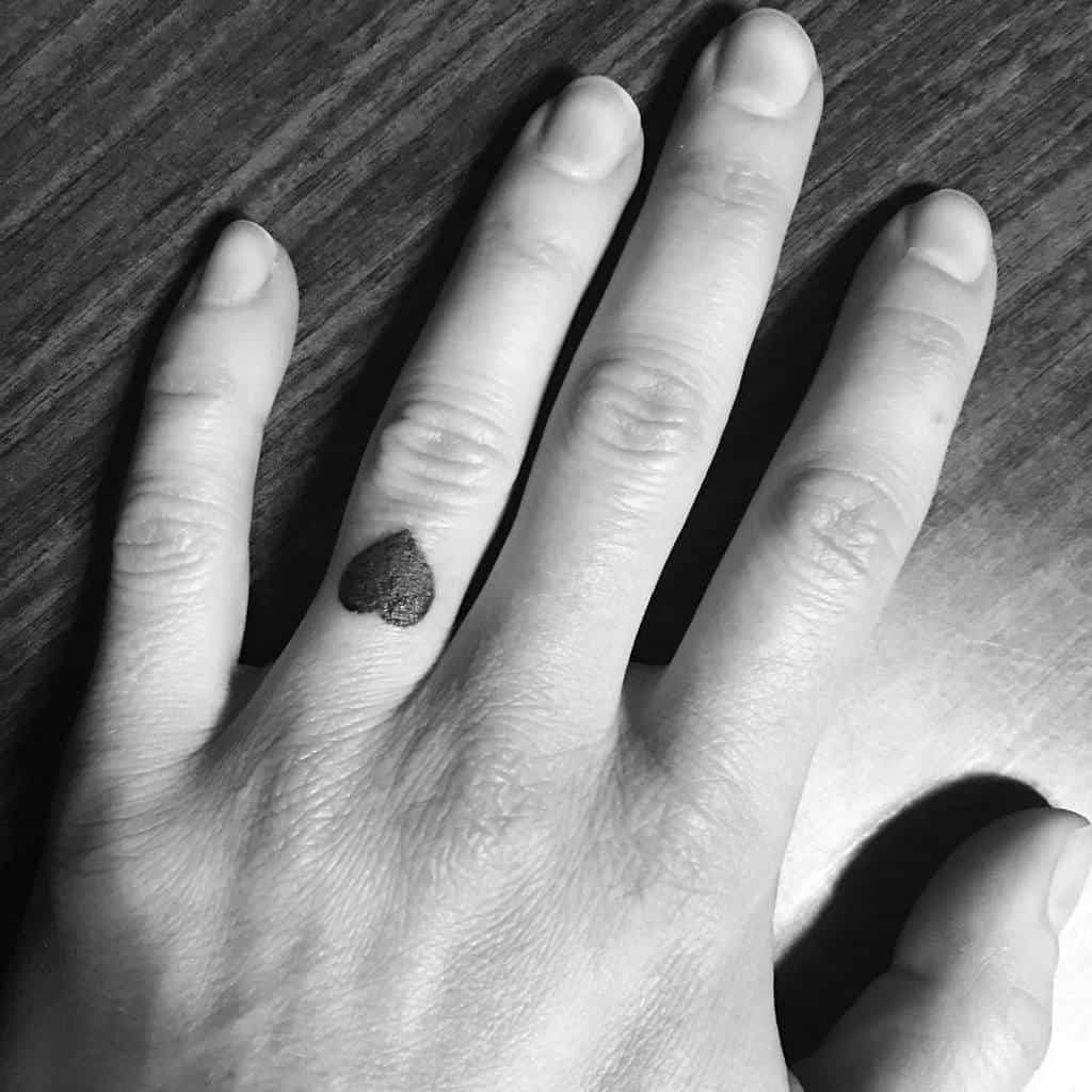 A hand with a small heart tattoo on the ring finger