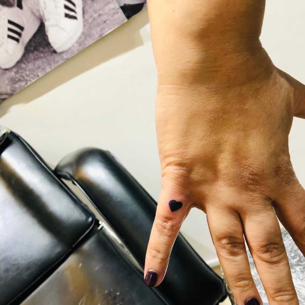 Hand with a small black heart tattoo on the finger
