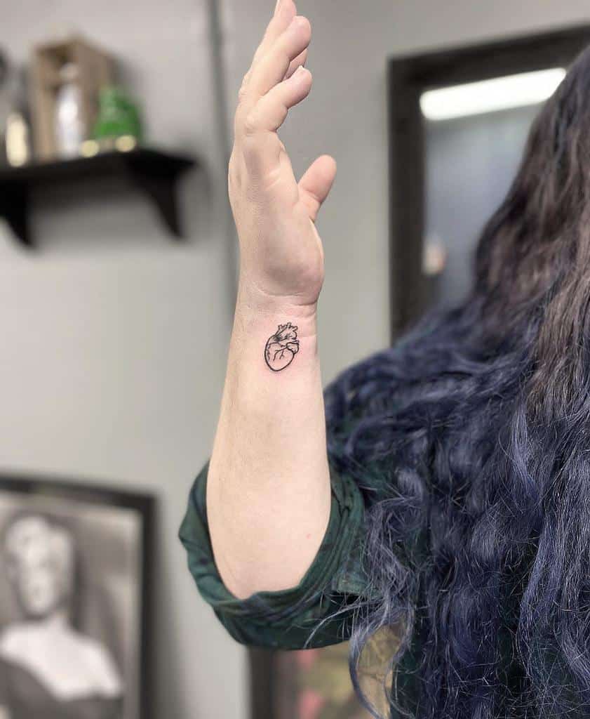 Person with a small heart tattoo on a raised forearm