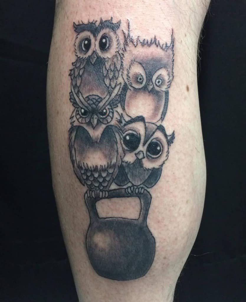 Tattoo of four majestic owls intricately stacked on a kettlebell, capturing the wisdom and strength embodied in these nocturnal creatures