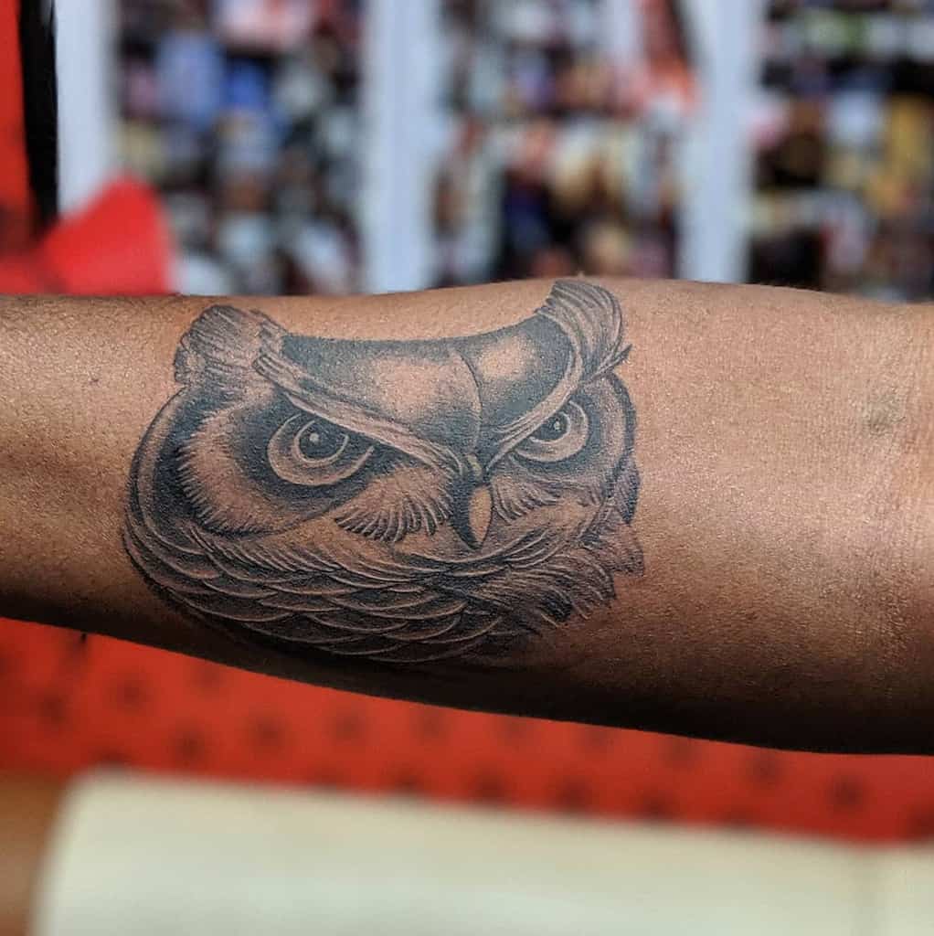 A captivating owl tattoo graces the person's forearm, showcasing intricate feather details and piercing, intense eyes