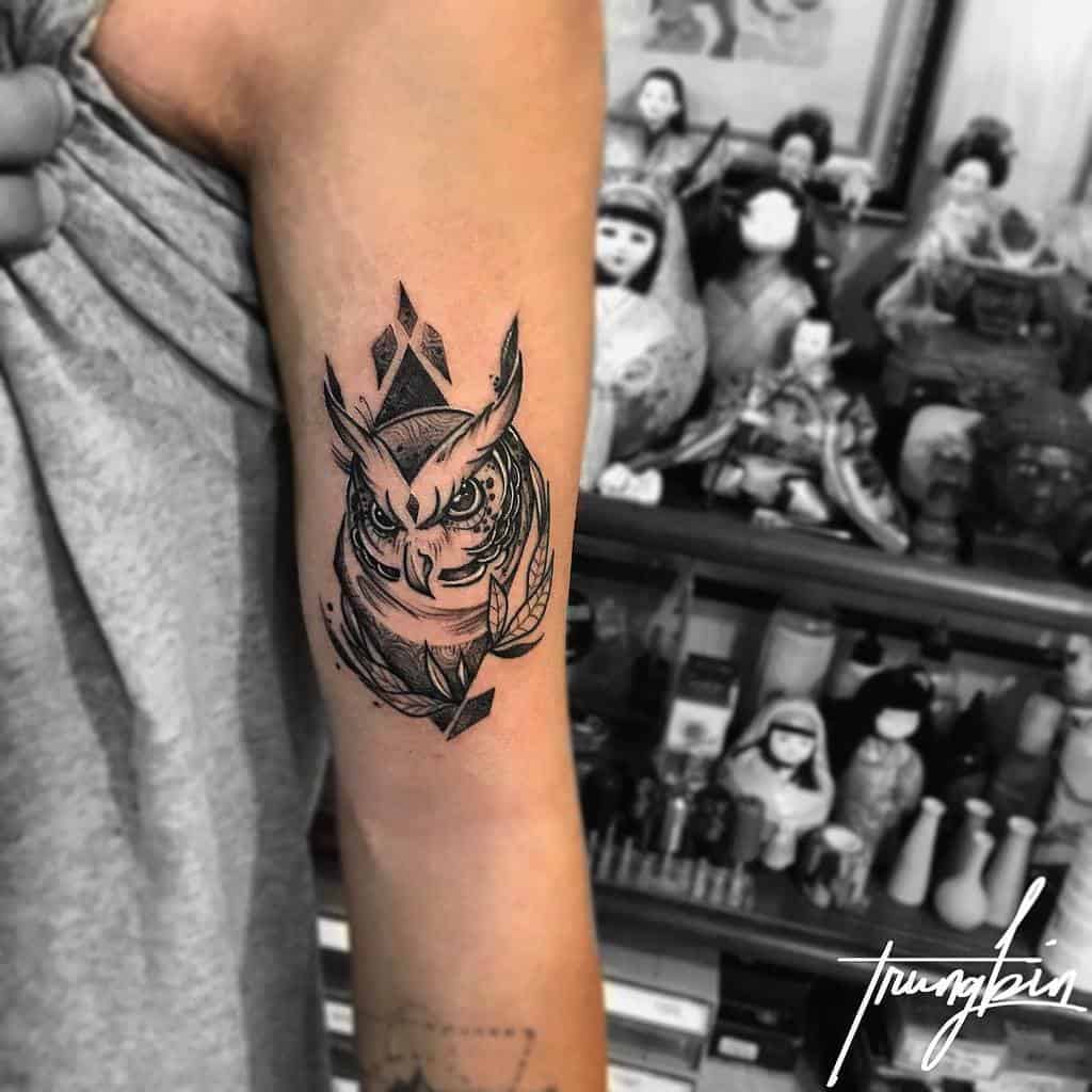 A black and white owl tattoo, designed with geometric shapes and sharp lines, symbolizing wisdom and strength, located on the upper arm