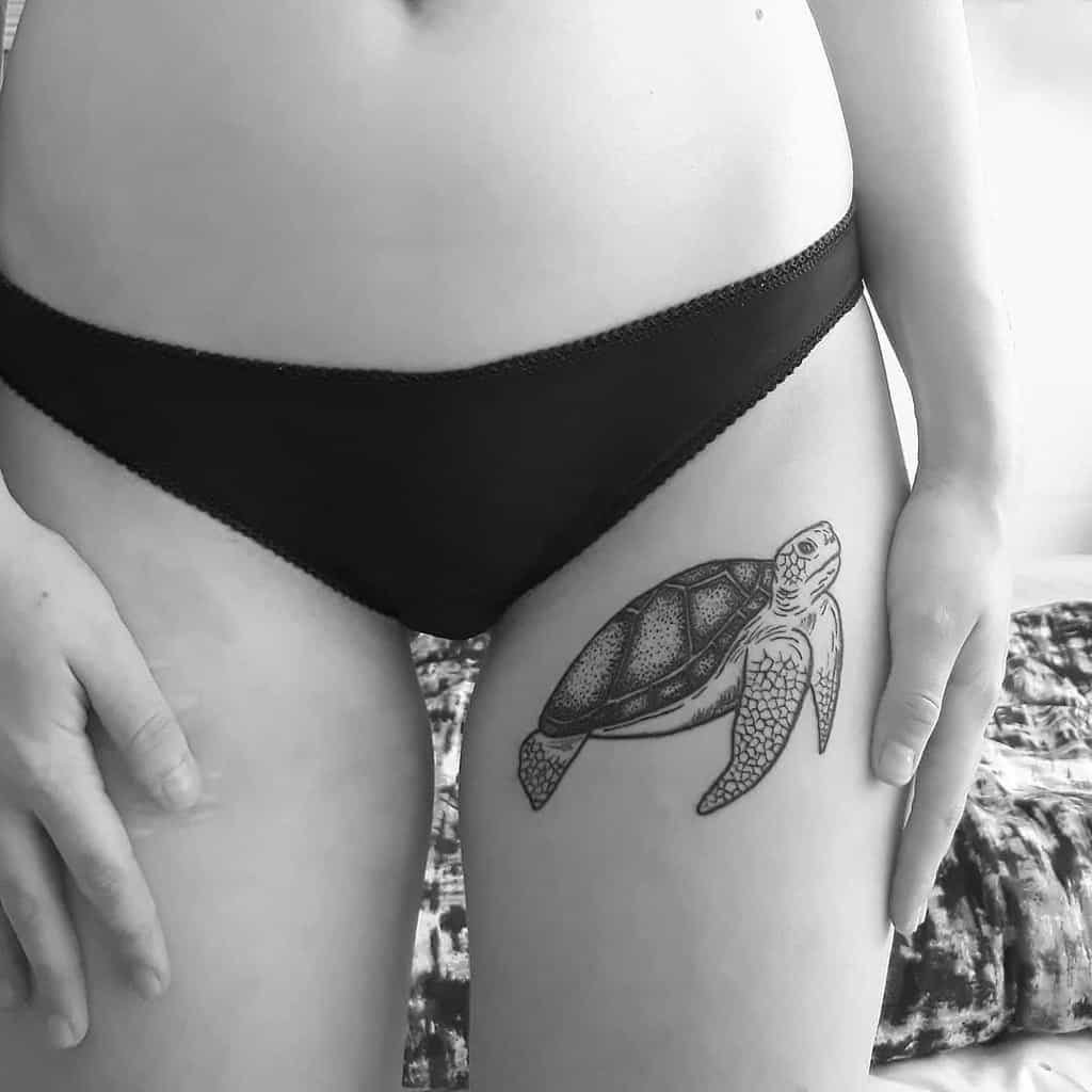A detailed black ink tattoo of a turtle swimming on the outer thigh, with intricate linework and dot shading