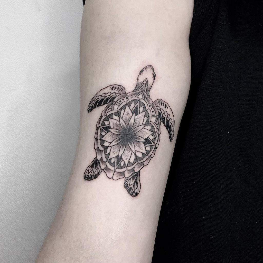 A tattoo of a turtle with a mandala design on an upper arm