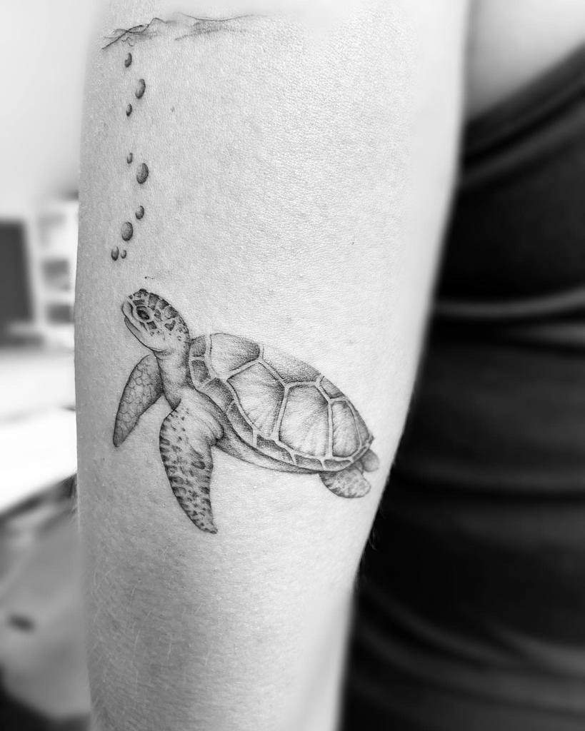 Tattoo of a sea turtle swimming with bubbles on an arm