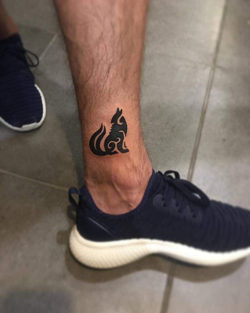 Minimalist black wolf tattoo on the ankle, featuring a sleek and elegant tribal-inspired design