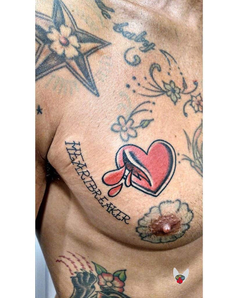 A chest adorned with various tattoos, including a bleeding heart with "HEARTBREAKER" written underneath