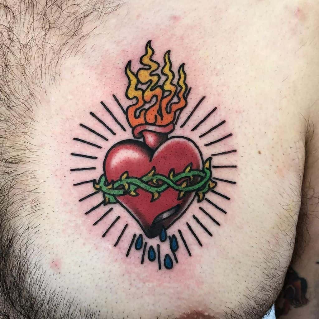 A tattoo of a Sacred Heart with flames, thorns, and blue droplets bleeding on a person's chest