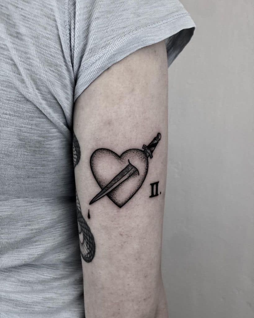 Tattoo of a dagger piercing a heart with a droplet, and the Roman numeral II on the upper arm