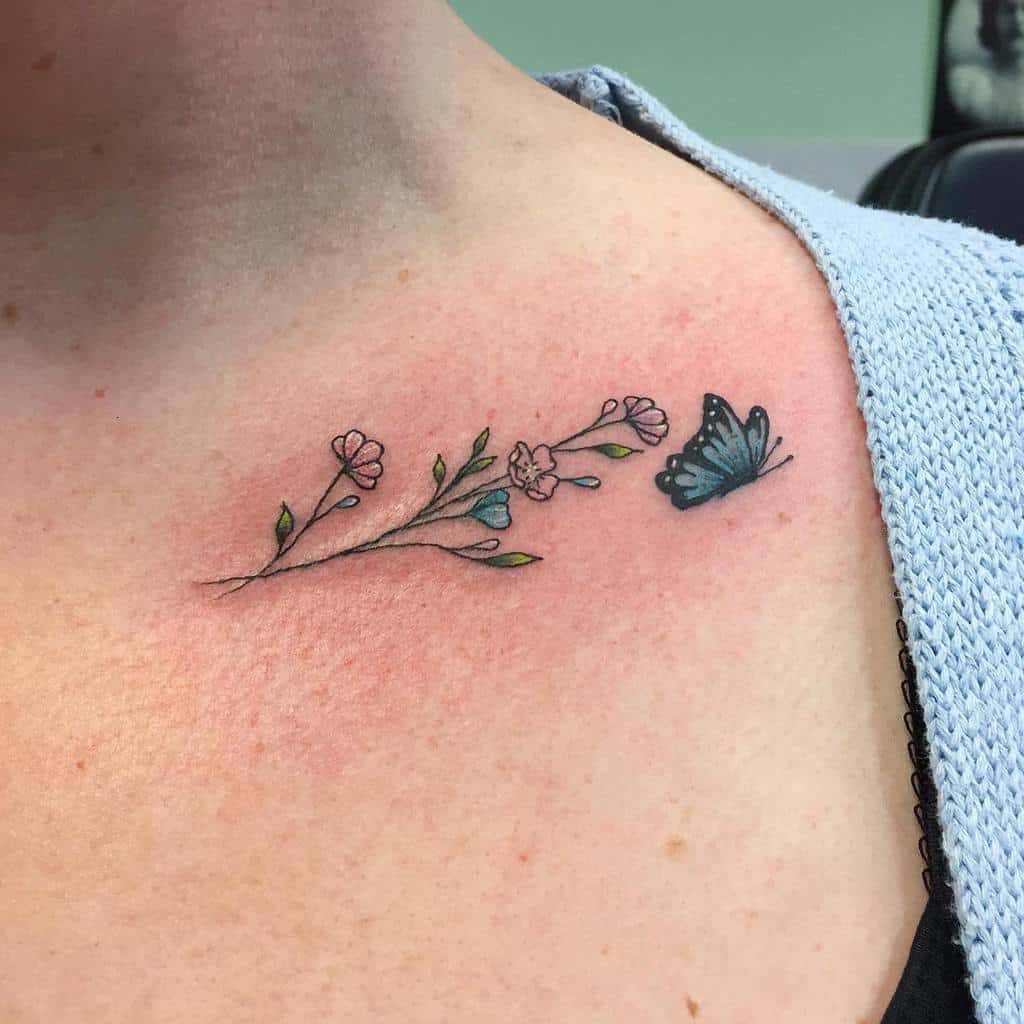 Tattoo of small pink flowers with a delicate blue butterfly on a person's collarbone