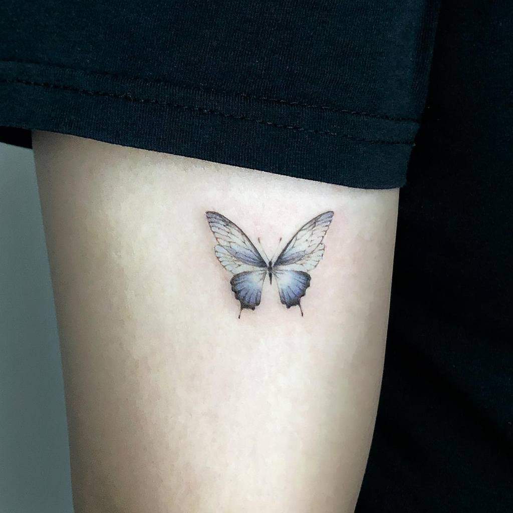 A detailed blue butterfly tattoo graces the arm