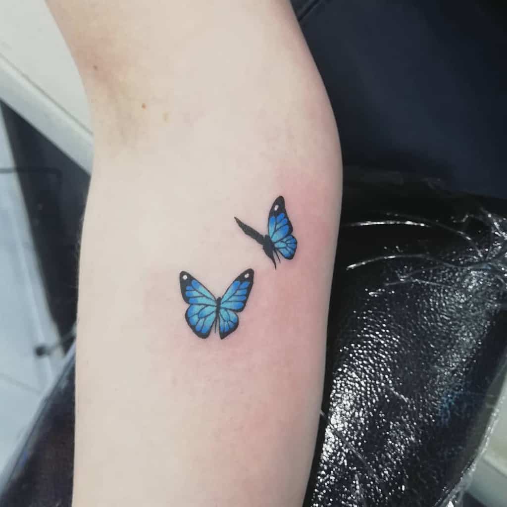 Two delicate blue butterflies tattooed on a forearm