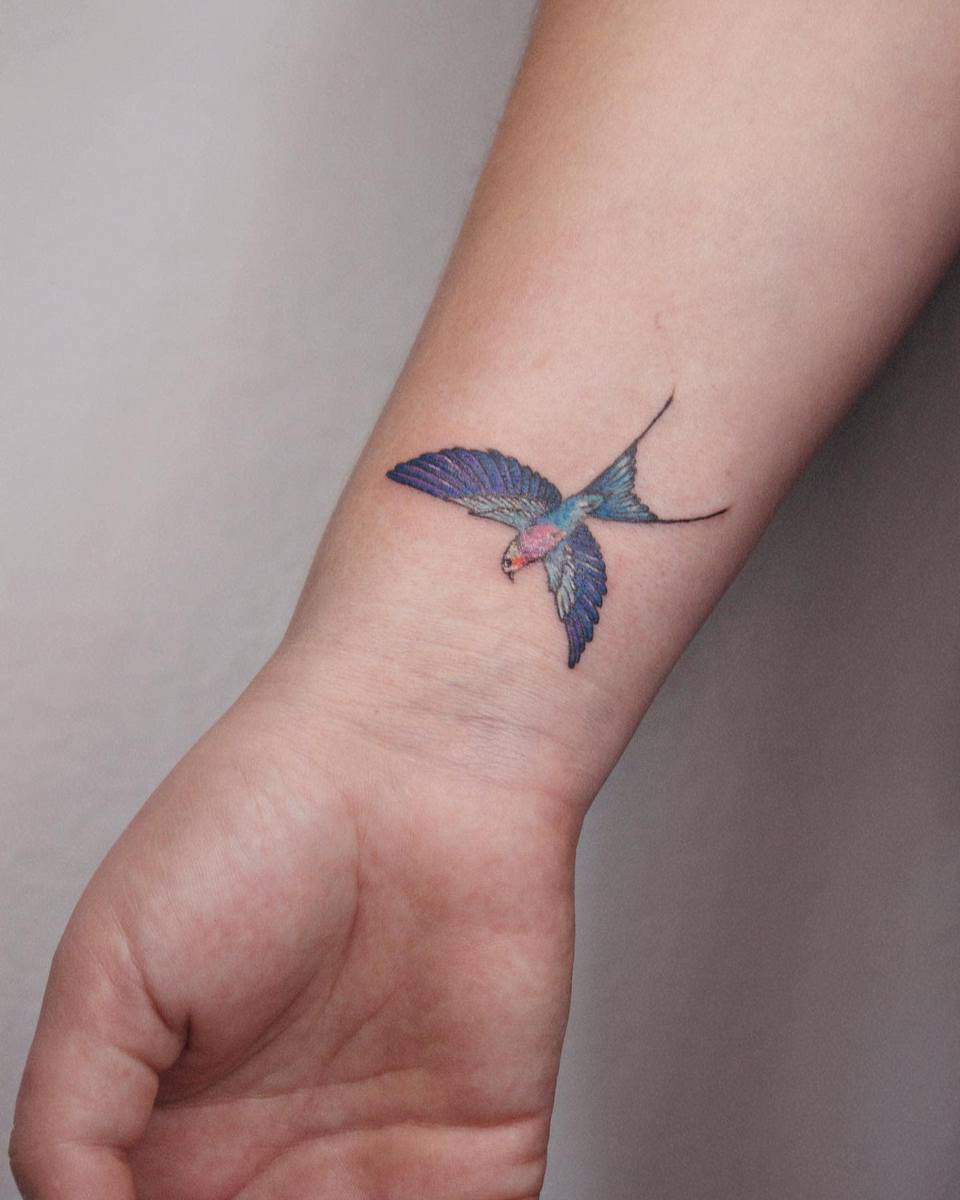 A small, colorful bird tattoo is inked on the inner wrist, appearing to be in flight