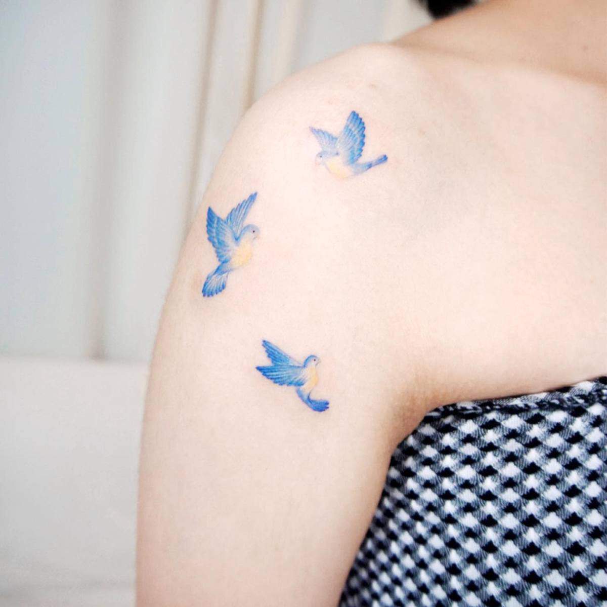 Three small blue birds tattooed on the upper arm wearing a checkered top